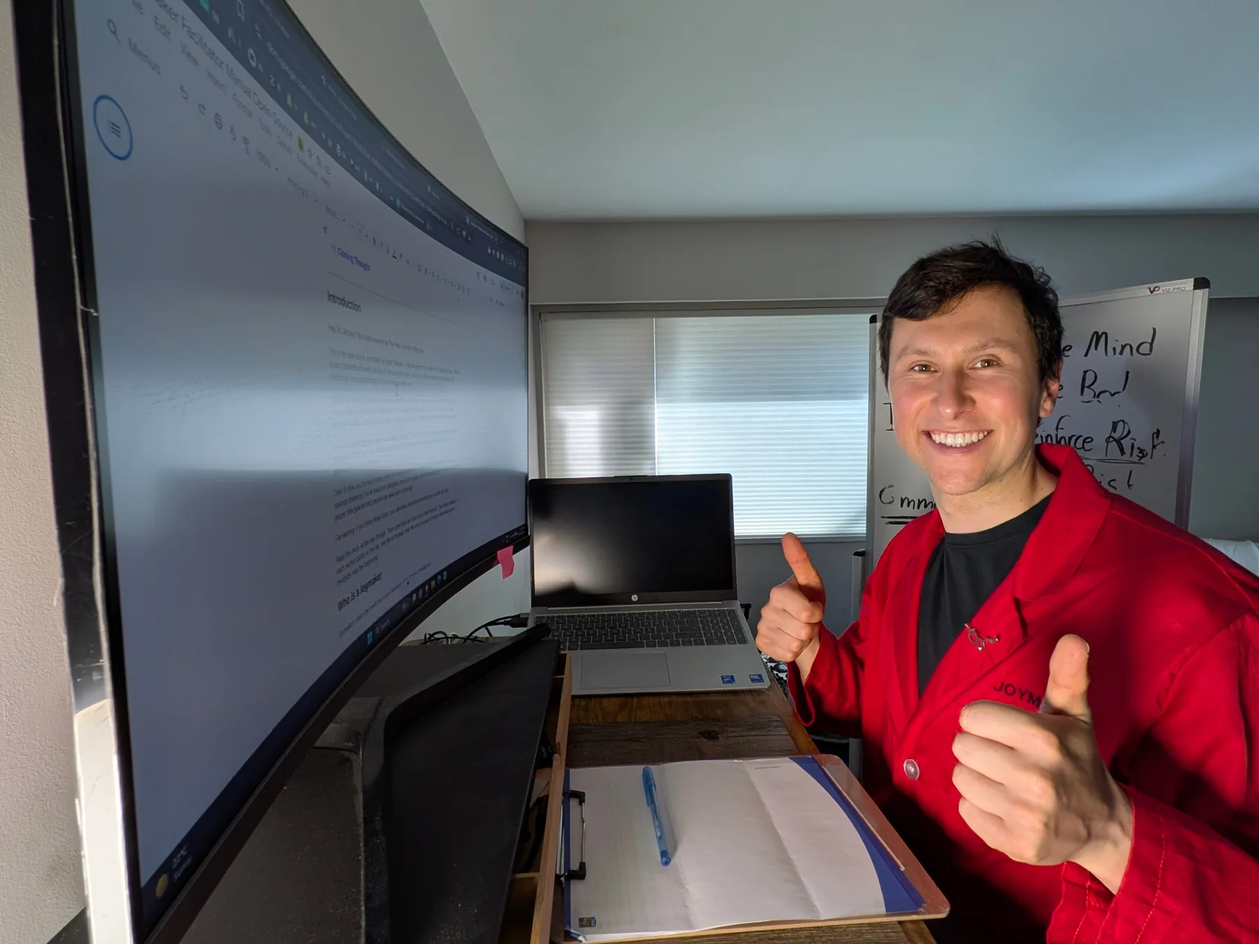 Jacques at his desk in the red Joymaker jacket, giving two thumbs up before an action call