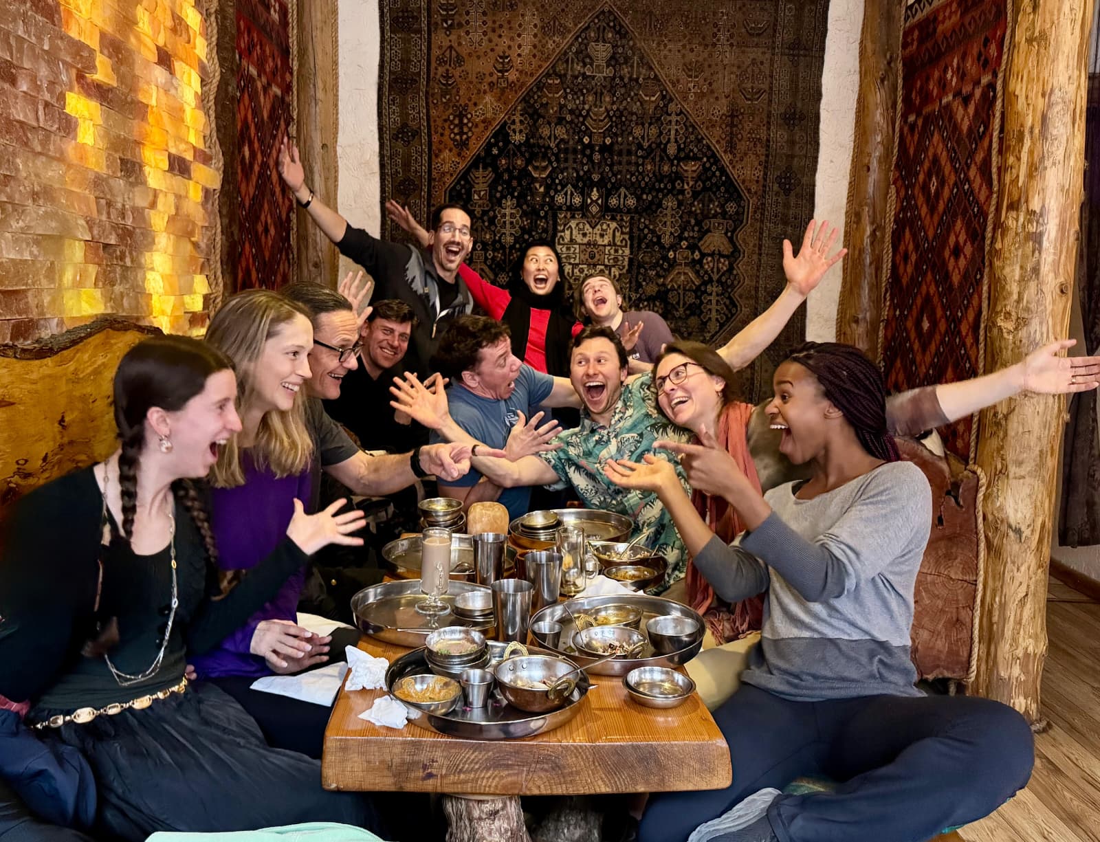 Long communal table piled with shared dishes, every face mid-laugh