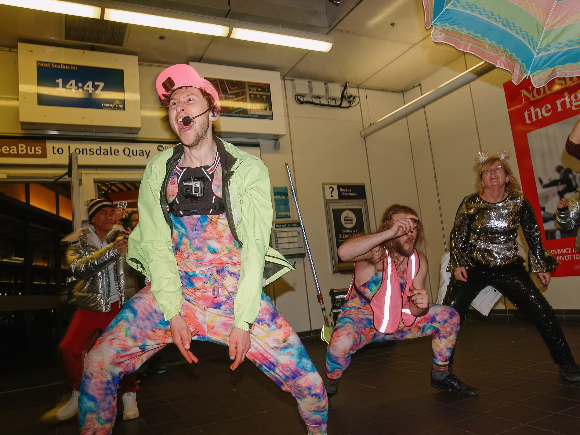 Performers in colourful jumpsuits dancing inside a transit station